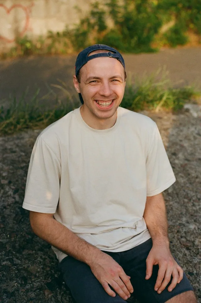 A young man sitting outside in evening light, smiling.